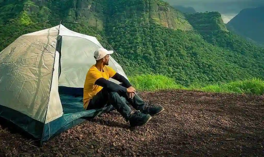 A boy sitting outside the camp which is pitched on the mountain.