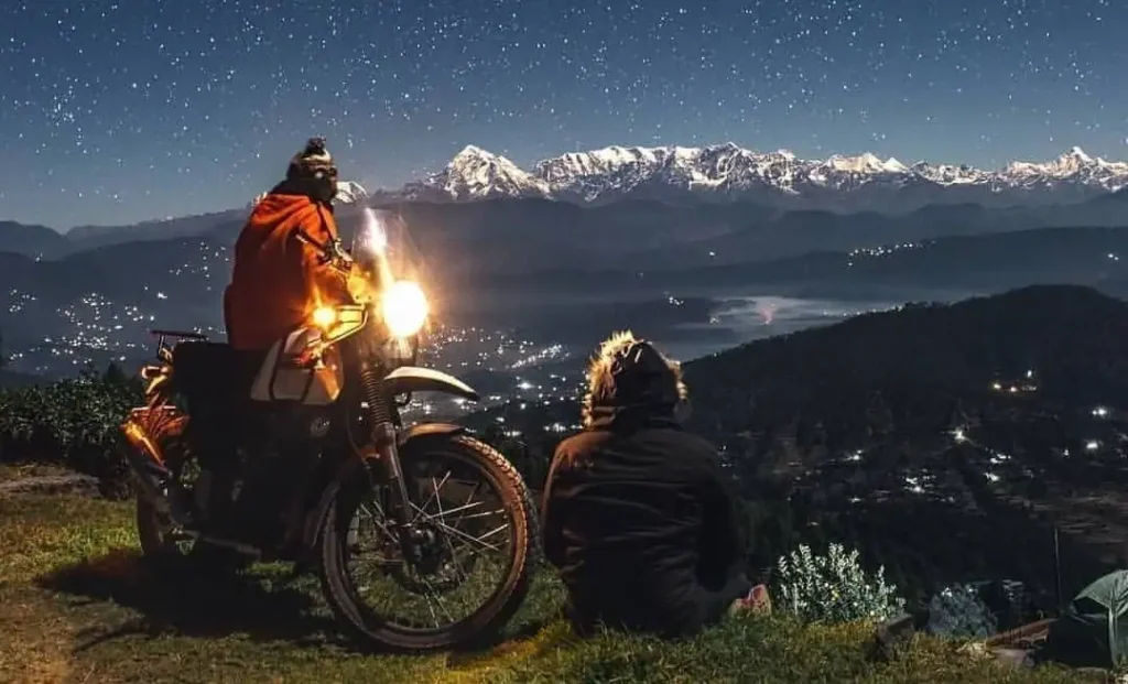 Two peoples standing on a cliff watching the view together with a bike