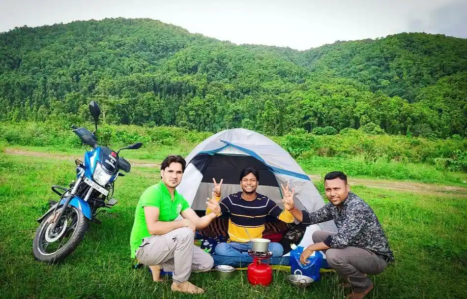 Three guys camping in a single tent and a bike is parked near it.